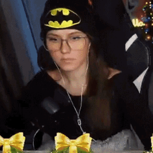 a woman wearing a batman hat and glasses is sitting in a chair with headphones on .