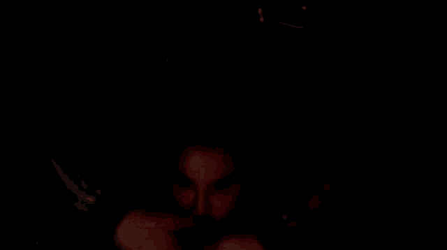 a man with a beard is looking out of a dark room with a red light shining on his face .