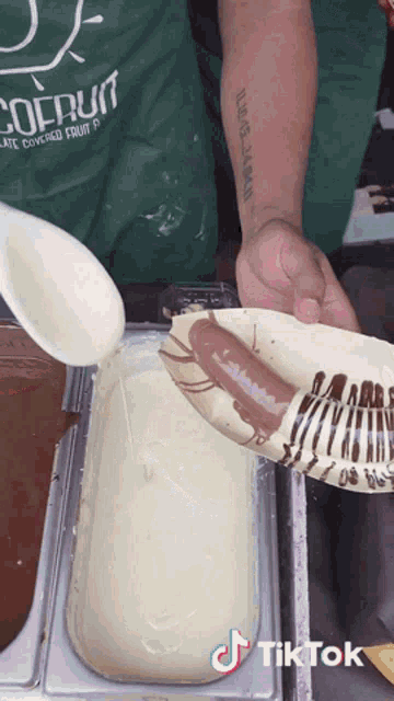 a man with a tattoo on his arm is pouring chocolate sauce into a container