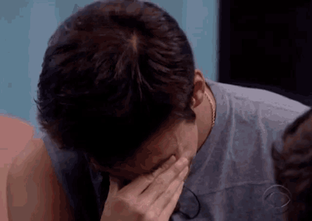 a man covering his face with his hand and a cbs logo in the corner