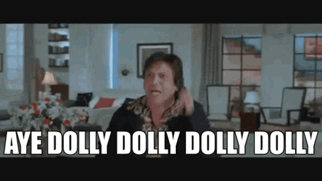 a man is sitting in a living room talking on a cell phone and saying aye dolly dolly dolly dolly .