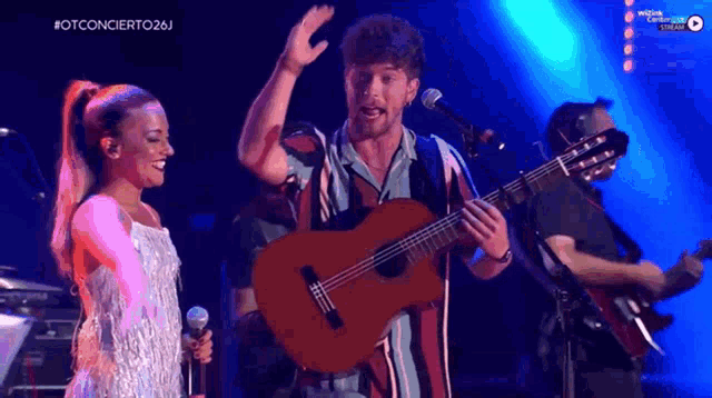 a man singing into a microphone while a woman holds a guitar