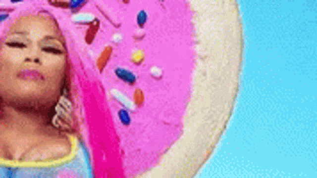 a woman with pink hair is standing in front of a pink cake with sprinkles on it .