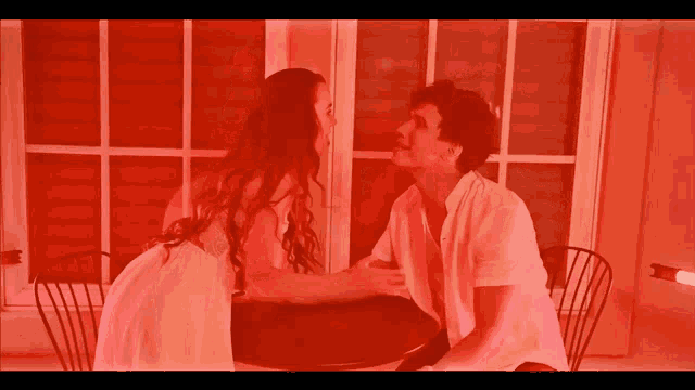 a man and a woman are sitting at a table in front of a red wall
