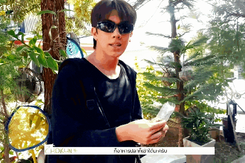 a man wearing sunglasses holds a piece of paper in front of a sign that reads chokun