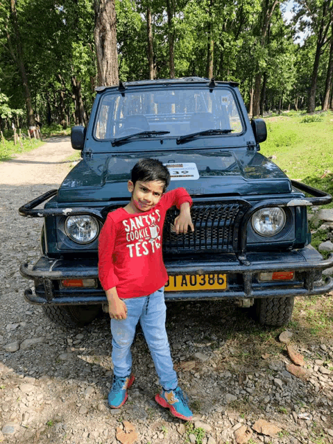 a boy wearing a santa 's cookie test shirt stands in front of a car