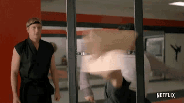 a man in a black karate uniform is standing next to another man in a netflix ad .