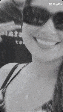 a woman wearing sunglasses is smiling in a black and white photo with the caption capcut