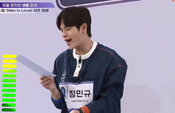a young man in a blue sweater is holding a piece of paper and singing .