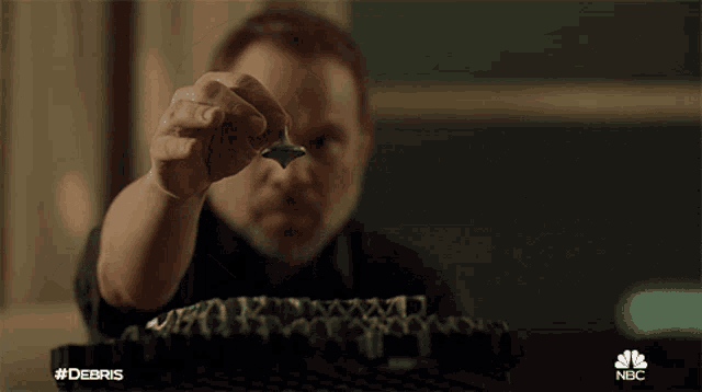 a man is holding a piece of metal in his hand with the nbc logo in the corner