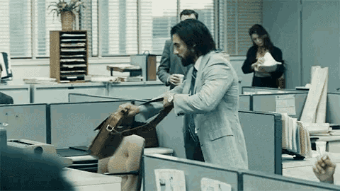 a man in a suit and tie is taking a purse out of a cubicle in an office .