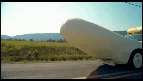 a white car is parked on the side of the road in front of a field with mountains in the background