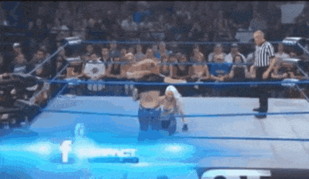 a man and a woman are wrestling in a wrestling ring with a referee watching .