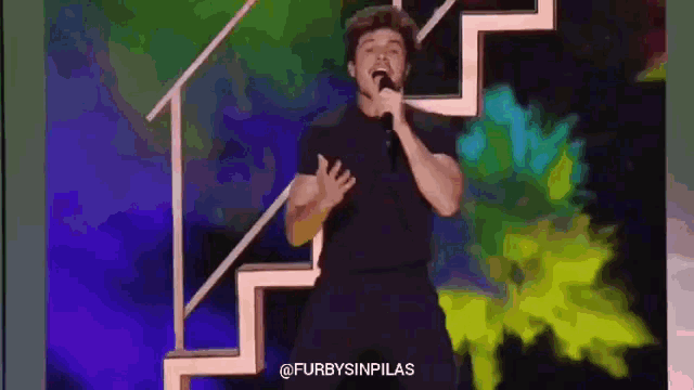 a man is singing into a microphone on a stage with stairs in the background .
