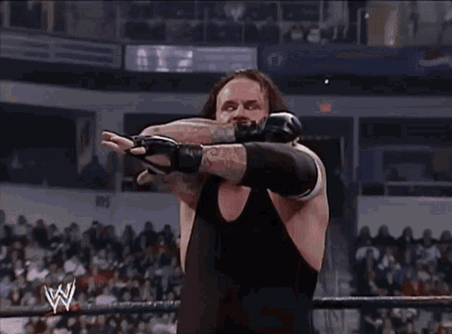 a wrestler with a tattoo on his arm is wearing a black tank top and gloves