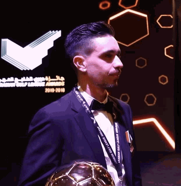 a man in a tuxedo is holding a soccer ball with a lanyard that says " dubai gold league " on it