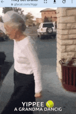 an older woman is holding a tennis ball and walking down the street