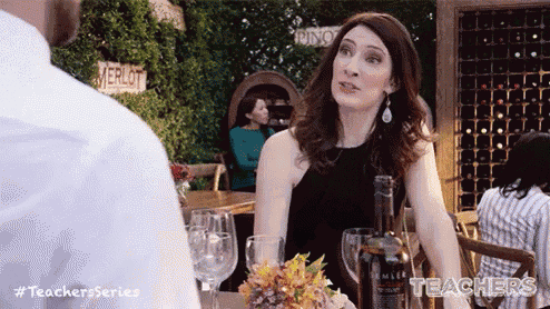 a woman in a black dress is sitting at a table with wine glasses and a bottle of wine .