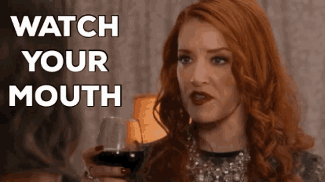 a woman with red hair is holding a glass of wine and says watch your mouth .