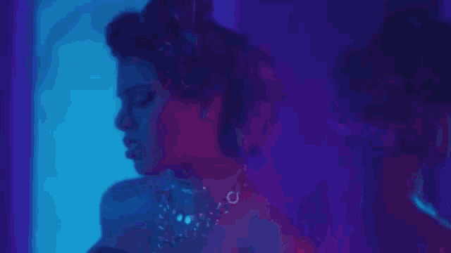 a woman in a dress is standing in front of a mirror in a room with purple lights behind her .