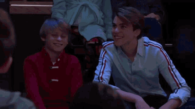 two young boys are sitting next to each other and smiling while watching a show .