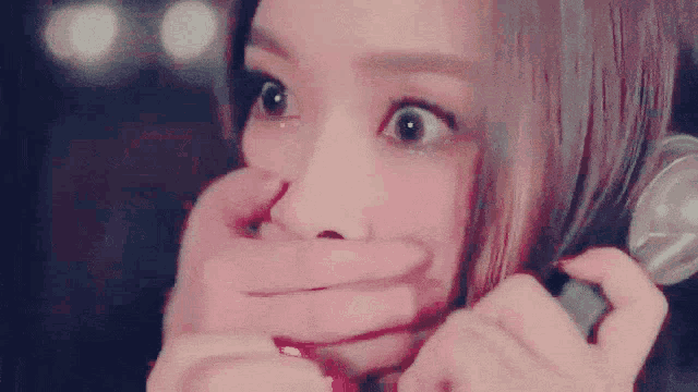 a woman is covering her mouth with her hand while talking on a telephone .