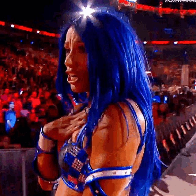 a female wrestler with blue hair is standing in front of a crowd .