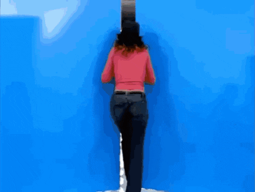 a woman in a pink sweater is walking through a blue doorway