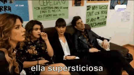 a group of people sitting on a couch with a sign that says ella supersticiosa on it