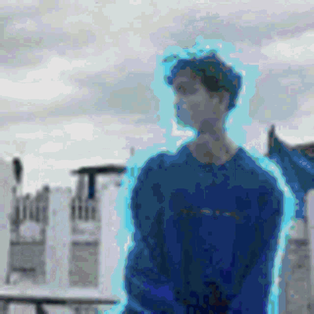 a man in a blue sweater is standing in front of a building with a blue glow around him .