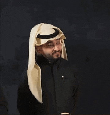 a man with a beard wears a black jacket and a white head scarf