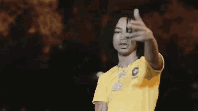 a man in a yellow shirt is making a funny face and pointing at the camera .