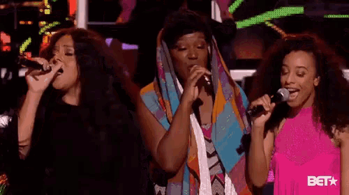 three women singing into microphones on a stage .