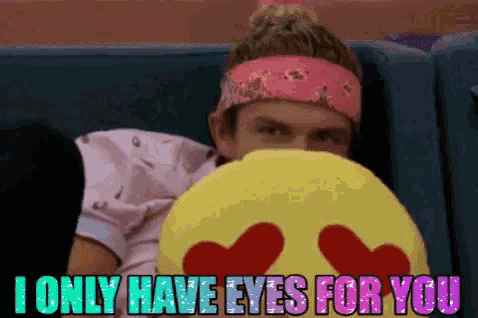 a man in a pink headband is hiding behind a yellow pillow with hearts on it
