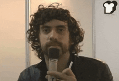 a man with curly hair and a beard is holding a microphone in front of him