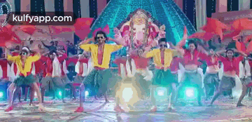 a group of people are dancing in front of a statue of ganesha on a stage .