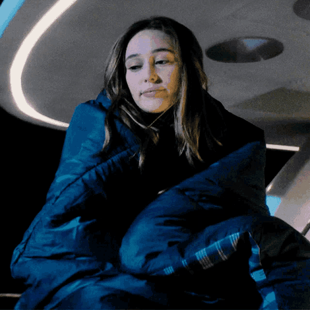a woman wrapped in a blue sleeping bag with a plaid blanket
