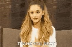 ariana grande is sitting on a couch and giving a thank you next sign .