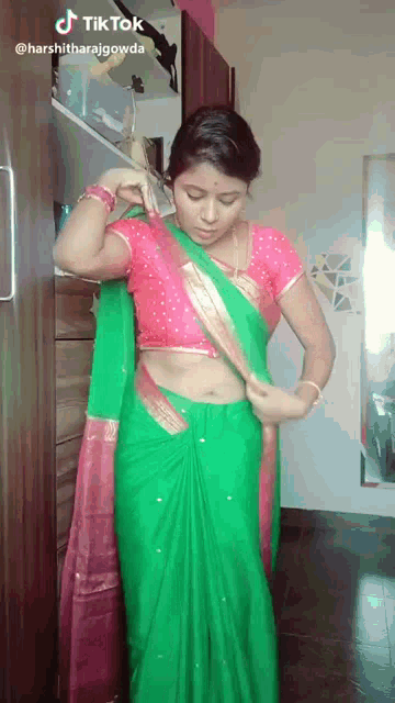 a woman in a green saree and a pink blouse is standing in front of a mirror .
