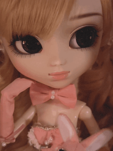 a close up of a doll wearing pink gloves and a pink bow