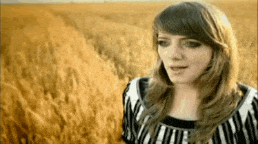 a woman in a striped shirt is standing in a field of tall grass