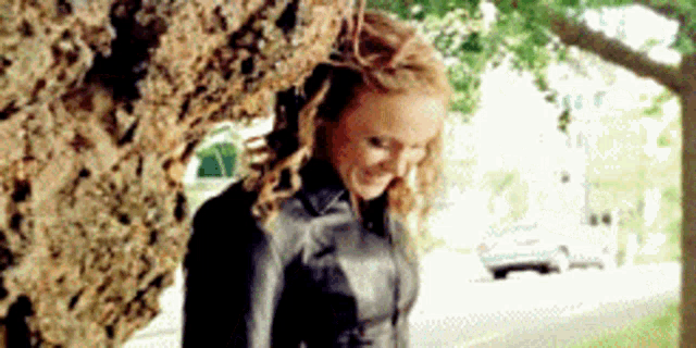 a woman is leaning against a tree and smiling .