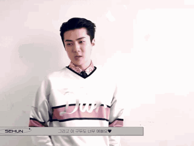a man is standing in front of a white wall wearing a white and pink sweatshirt .