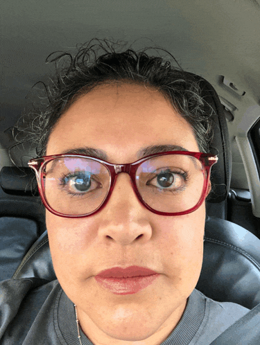 a woman wearing glasses and a gray shirt looks at the camera