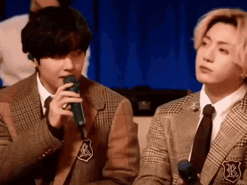 two men in suits and ties are sitting next to each other . one of the men is holding a microphone .
