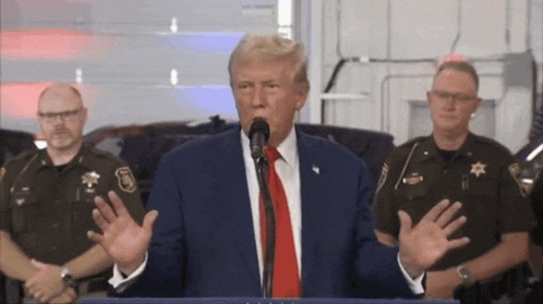 a man in a suit and tie is speaking into a microphone with a sheriff behind him