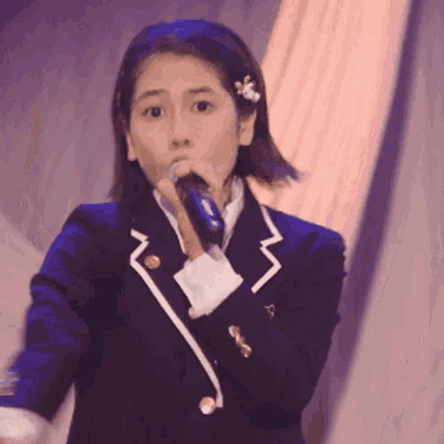 a girl in a school uniform is singing into a microphone on stage .