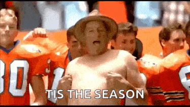 a shirtless man in a cowboy hat stands in front of a group of football players with the words tis the season behind him