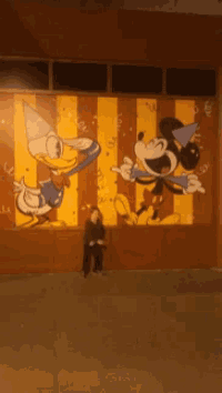 a boy stands in front of a painting of mickey mouse and donald duck