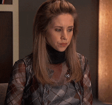a woman wearing a plaid shirt and a black turtleneck looks at the camera